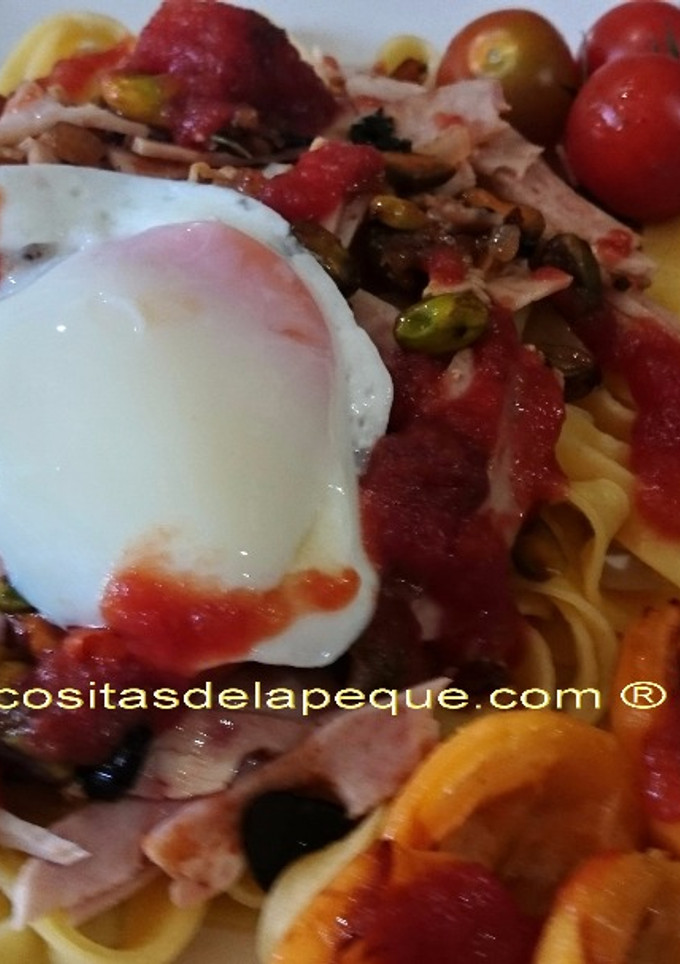 Una foto de Pappardelle con sofrito de tomatitos cherri, ajo negro y pistachos, acompañado de huevo a baja temperatura