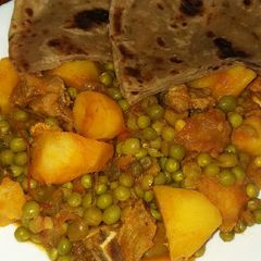 A picture of Beef stew with potatoes and green peas.