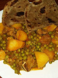 A picture of Beef stew with potatoes and green peas.