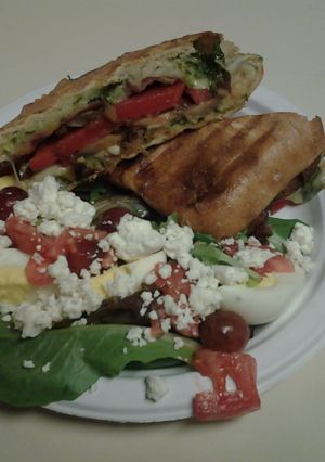 A picture of Ciabata bread, pesto, pepper, and cheese sandwich with spinach salad.