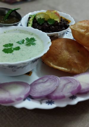 A picture of Kale chane, bathua ka raita with poori.