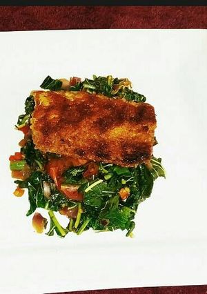 A picture of Grilled breaded Fish filet on a bed of Blanched Spinach.
