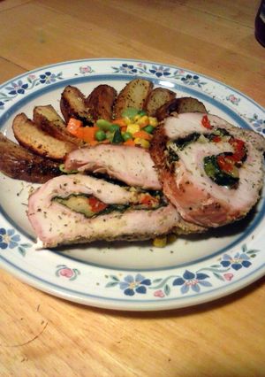 A picture of spinach and pepper stuffed pork loin with parmesan potato wedges and mixed veggies.