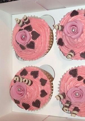 A picture of pink rose cupcakes with pink buttetcream, chocolate swirls & hearts.
