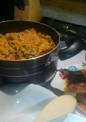 A picture of Jollof rice with veggies with peppered chicken and goat meat.