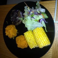 A picture of venison burger topped with sweet onions with aside of sweet potato mash with sweet corn.