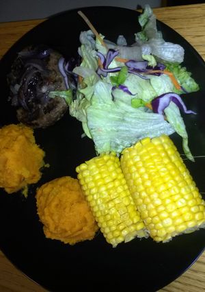 A picture of venison burger topped with sweet onions with aside of sweet potato mash with sweet corn.
