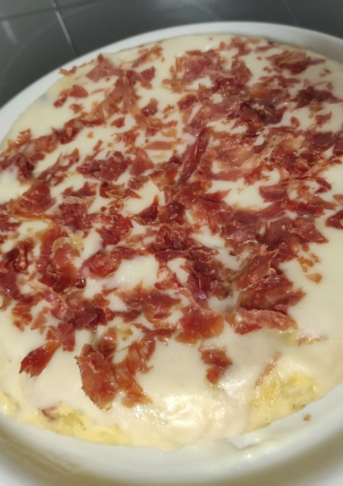 Una foto de Tortilla de patatas rellena de jamón serrano y topping de alioli y jamón crujiente