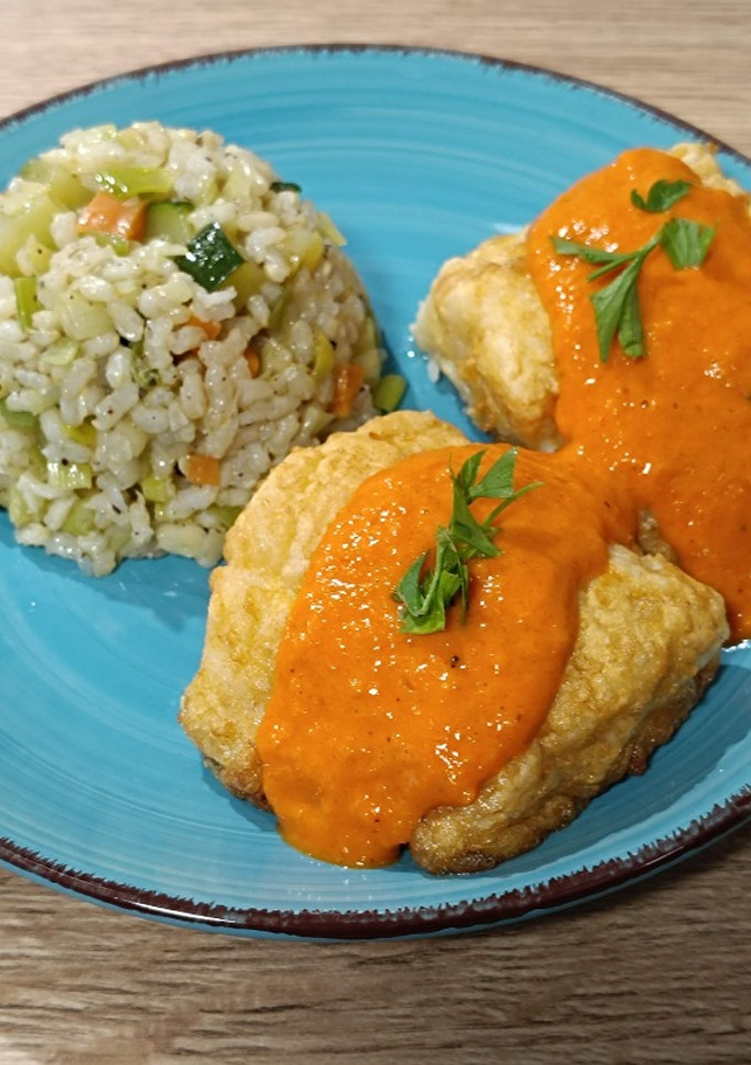 Una foto de Bacalao rebozado con salsa de piquillo y guarnición de arroz con verduras