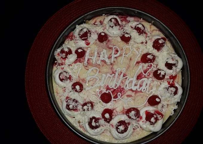 White chocolate raspberry swirl cheesecake topped with raspberries and sauce