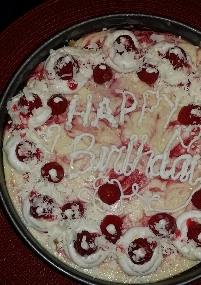A picture of White chocolate raspberry swirl cheesecake topped with raspberries and sauce.