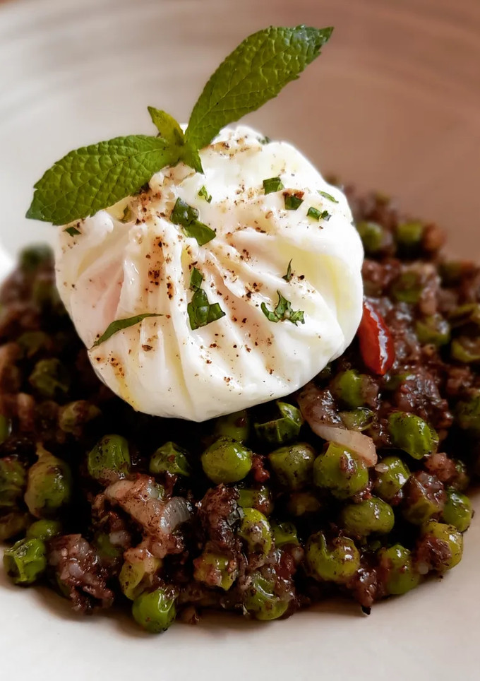 Una foto de Guisantes picantitos con morcilla y menta y huevo poché