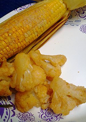 A picture of Oven roasted corn unhusked and cauliflower.
