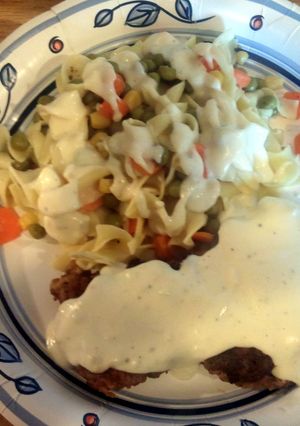 A picture of chicken fried steak with gravy and egg noodles.
