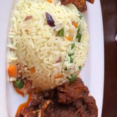 A picture of Fried rice and goat meat sauce and fried plantain.