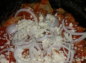 Una foto de Chilaquiles rojos con cebolla y queso