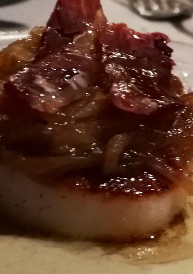 Una foto de Vieira sobre parmentier de alcachofa, con cebolla caramelizada y crujiente de ibérico
