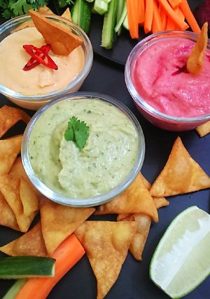 A picture of Nachos with 3 different hummus dips.