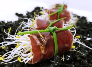 Una foto de Rollitos de cecina con germinados y sirope de membrillo sobre tierra de aceitunas negras y aceite aromatizado de romero