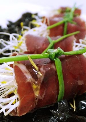 Una foto de Rollitos de cecina con germinados y sirope de membrillo sobre tierra de aceitunas negras y aceite aromatizado de romero