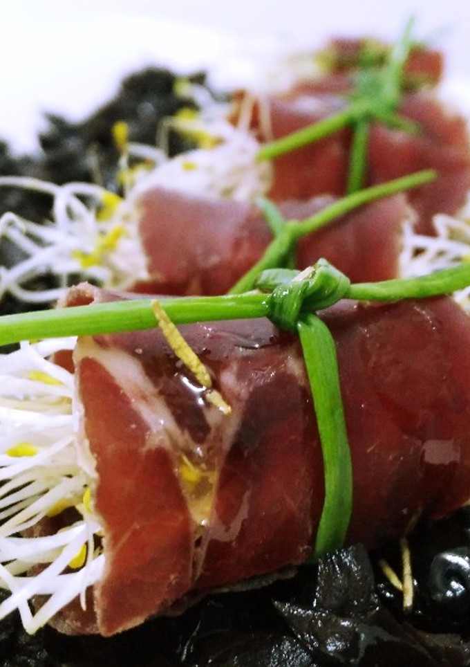 Una foto de Rollitos de cecina con germinados y sirope de membrillo sobre tierra de aceitunas negras y aceite aromatizado de romero