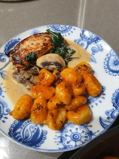 Una foto de Ñoquis al pesto rojo con pechuga de pollo marinada en salsa de champiñones con espinacas