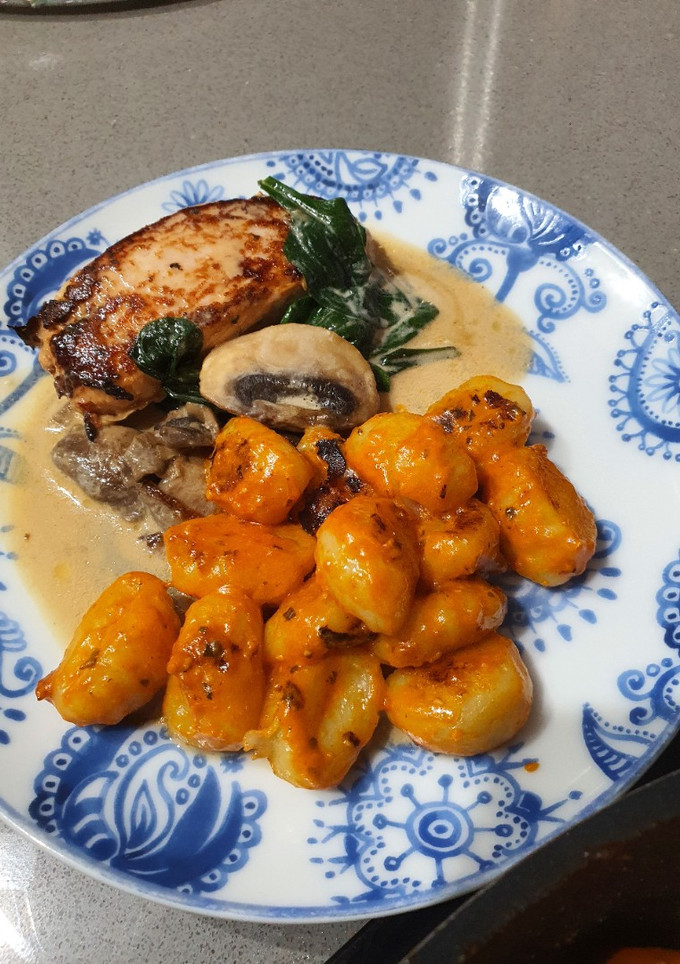 Una foto de Ñoquis al pesto rojo con pechuga de pollo marinada en salsa de champiñones con espinacas