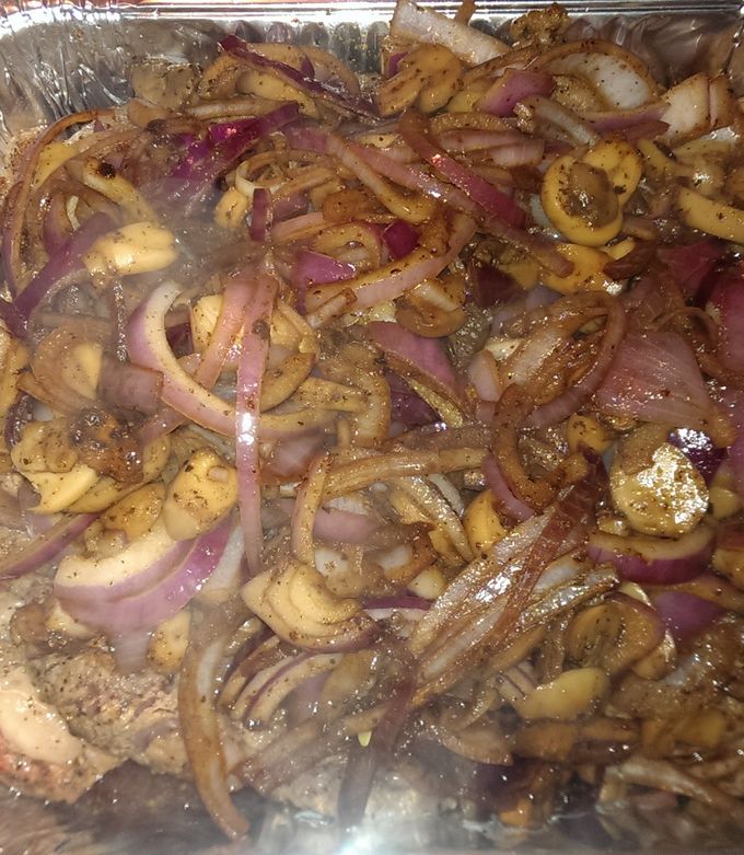 A picture of Ribeye steak smothered in onions and mushrooms.