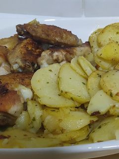 Una foto de Alitas y muslos de pollo con patatas y salsa verde