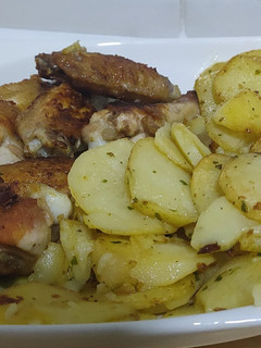 Una foto de Alitas y muslos de pollo con patatas y salsa verde