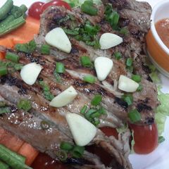 A picture of Moo Kam Waan / Thai style Grilled Pork serve with Spicy Sauce and fresh vegetables.