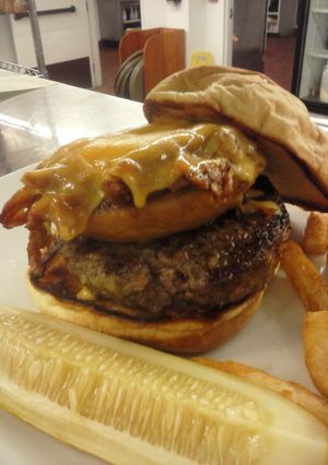 A picture of Beef Tender loin burger with pulled pork stuffed onion ring and melted cheddar cheese.
