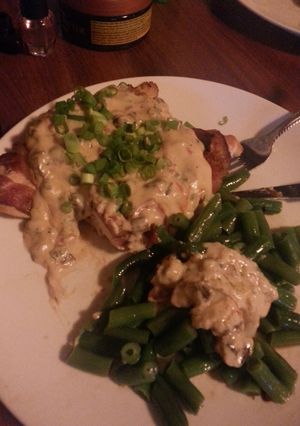 A picture of Bacon wrapped chicken w/Roma tomatoes, mushrooms, green onions in alfredo sauce.