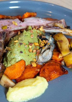 Une photo de Agneau laqué, huitre snackée, condiment avocat, condiment agrumes et poêlée de légumes