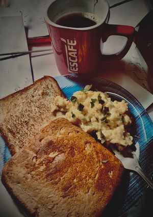 A picture of Scrambled eggs paired with toast and a cup of black coffee.
