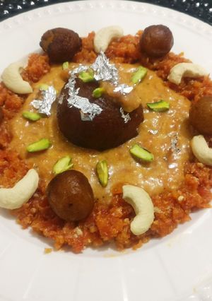 A picture of Stuffed cheese gulab jamun in carrot shahi rabri.