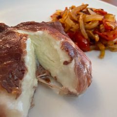 A picture of Oven Baked Mozzarella wrapped in Parma Ham, with sautéed Onion and Tomato.