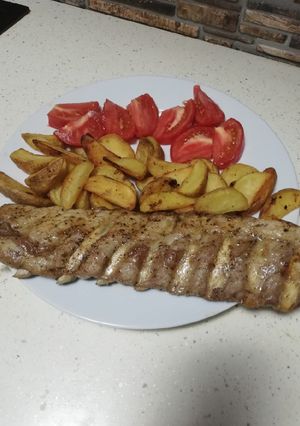 O poză a rețetei Coastă de porc la cuptor cartofi wedges și o roșie tăiată.