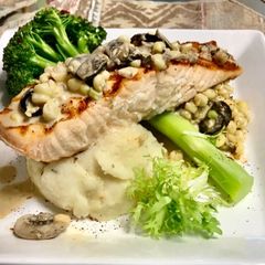 A picture of Grilled salmon Topped with a mushroom, Black olives, White corn cream sauce Garlic Mashed potatoes.