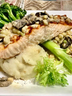 A picture of Grilled salmon Topped with a mushroom, Black olives, White corn cream sauce Garlic Mashed potatoes.