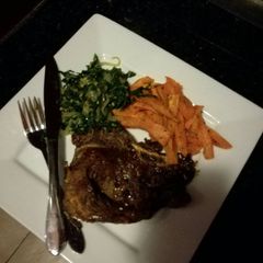 A picture of T-bone steak,sweet potato chips and sauteed spinach with onions.