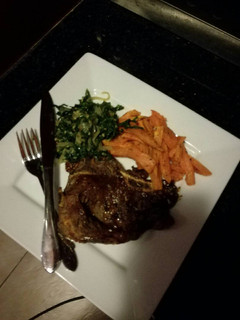 A picture of T-bone steak,sweet potato chips and sauteed spinach with onions.