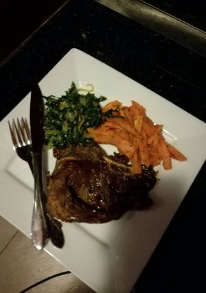 A picture of T-bone steak,sweet potato chips and sauteed spinach with onions.