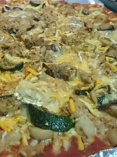 Una foto de Pizza de tomate frito, calabacín, berenjena, queso rulo de cabra, champiñones y atún