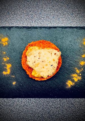 Une photo de Scampis au curcuma sur galettes de quinoa et de tapenade de poivron - tuile au parmesan