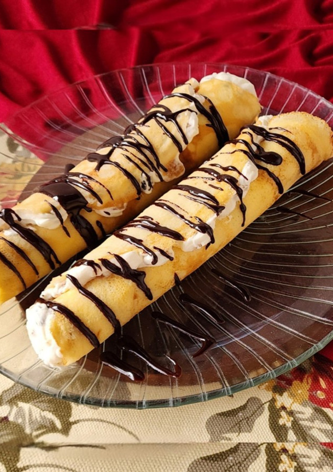 Una foto de 🫔Panqueques rellenos de manzana, pasas y crema, bañados con salsa de chocolate🫔 Canelones dulces