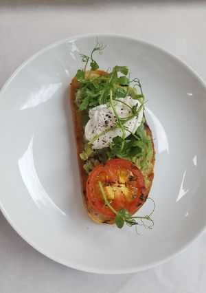 A picture of Soft Poached egg smashed avocado grilled tomato on sourdough.
