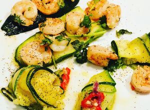 Una foto de Langostinos al Ajillo y Cayena acompañados de Láminas de Zucchini en aceite Picoso