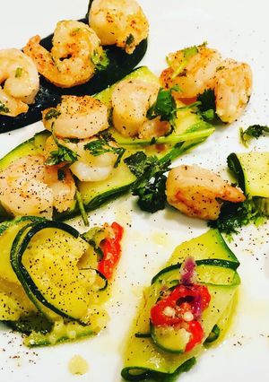 Una foto de Langostinos al Ajillo y Cayena acompañados de Láminas de Zucchini en aceite Picoso