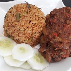 A picture of Jollof rice with fried chicken and cucumber.